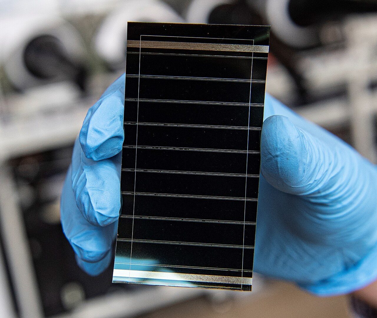 A gloved hand holding a small perovskite solar cell.
