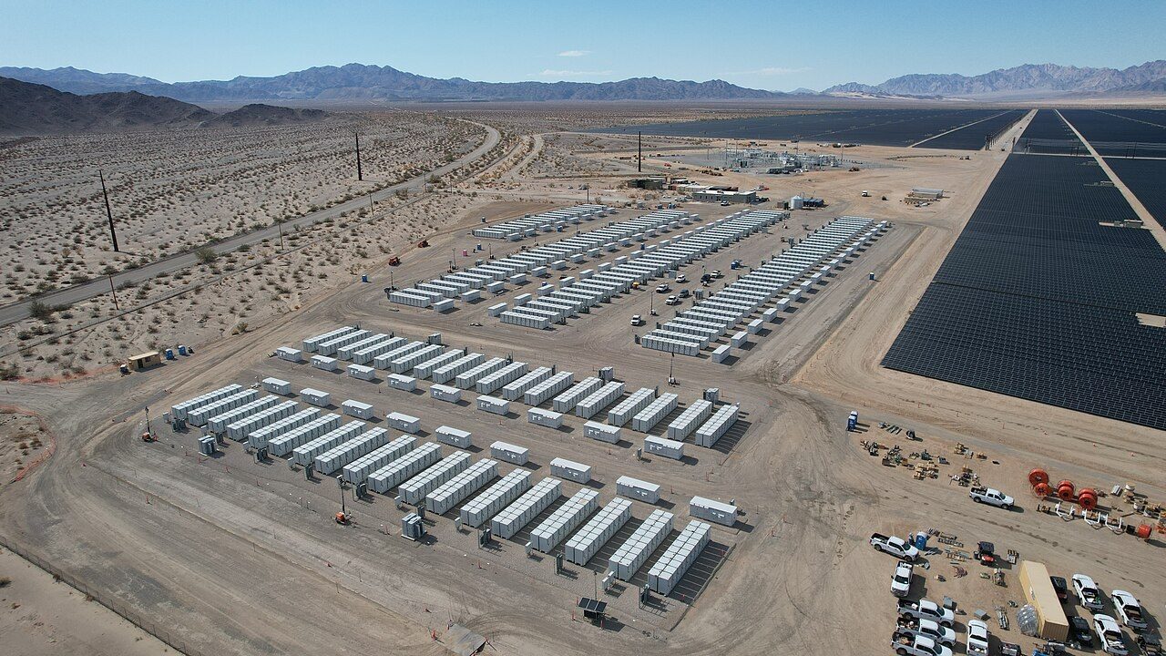 A grid battery storage site next to the Desert Sunlight solar farm in Riverside County, California, with rows of battery units, a substation and power lines.