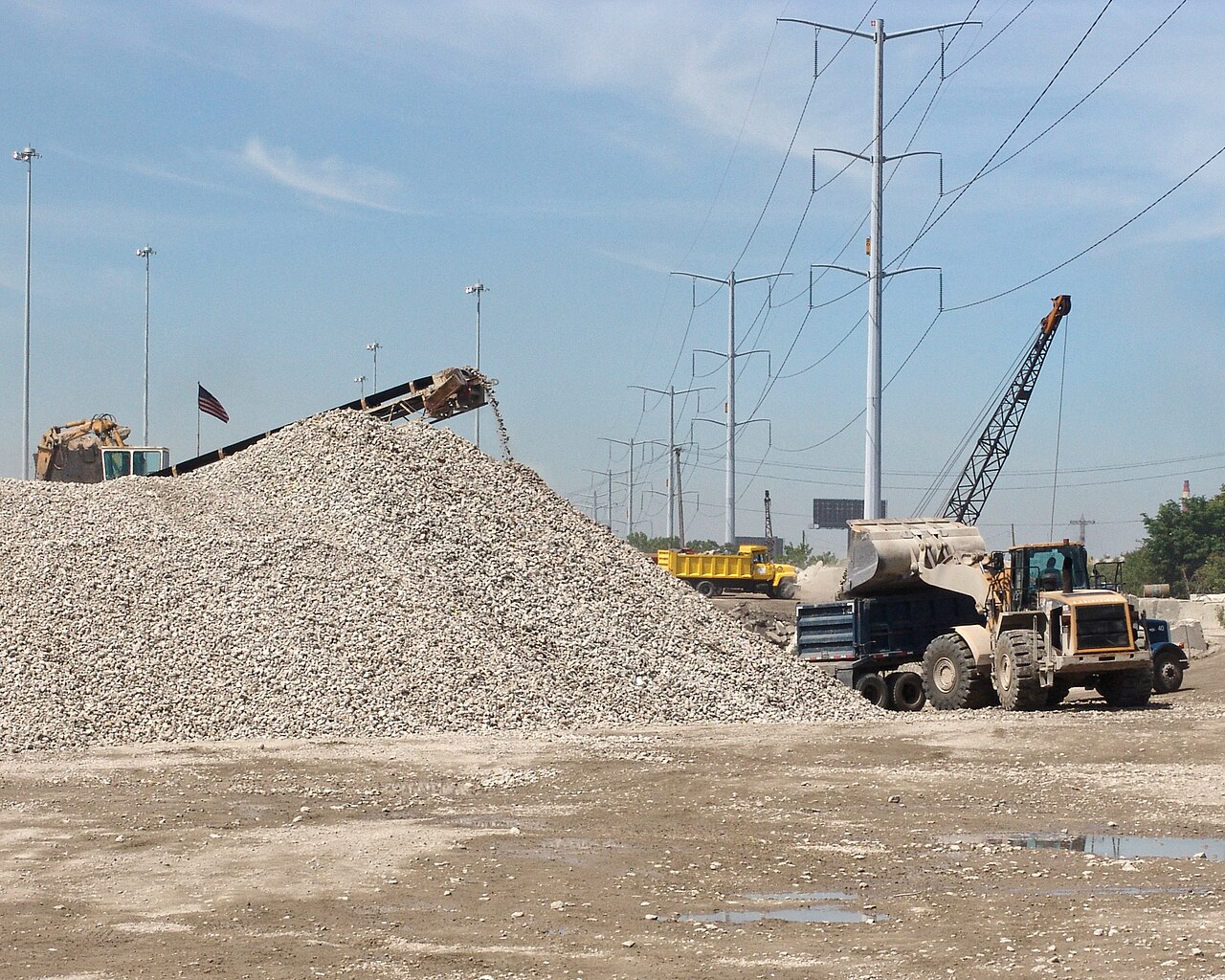 A conveyor feeding a pile of crushed concrete aggregate beside a loader
