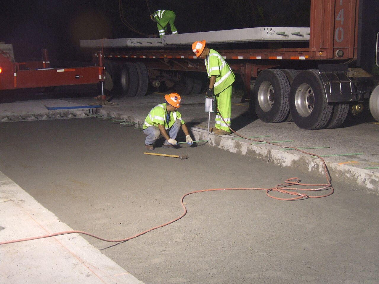 Highway workers installing tie bars in a freshly placed light-colored concrete pavement slab