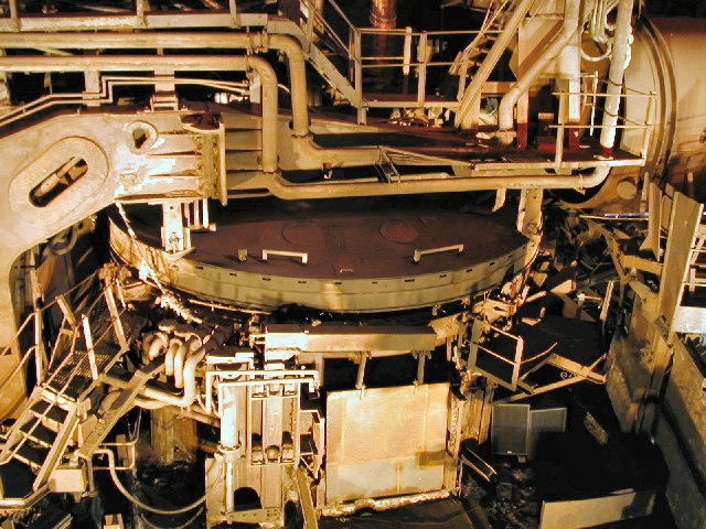 Interior of an electric-arc furnace hall with a circular furnace lid, pipes, and walkways