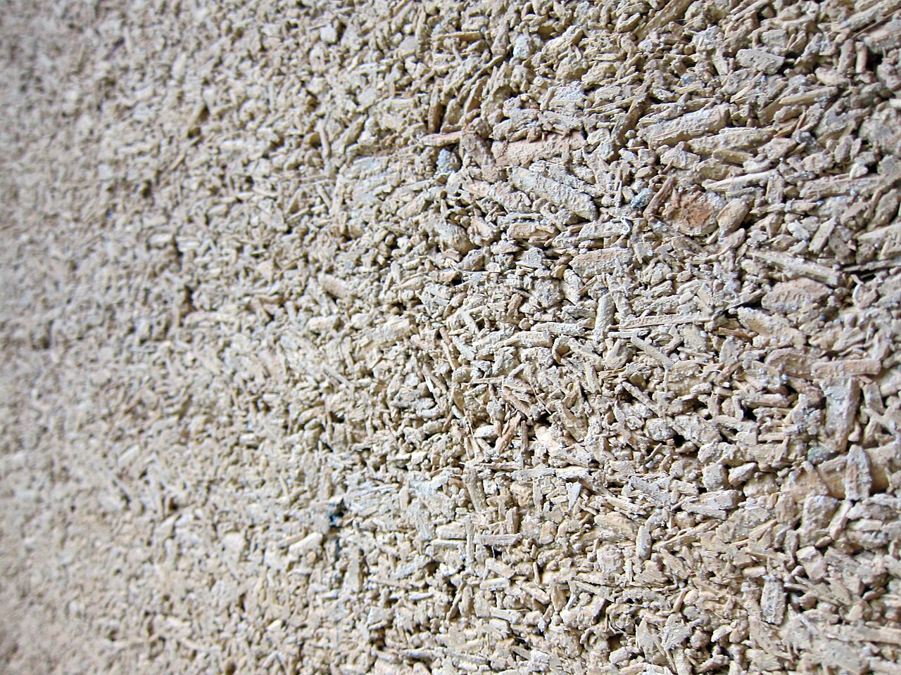 Close-up of a hempcrete wall: pale lime binder packed around short hemp hurd chips