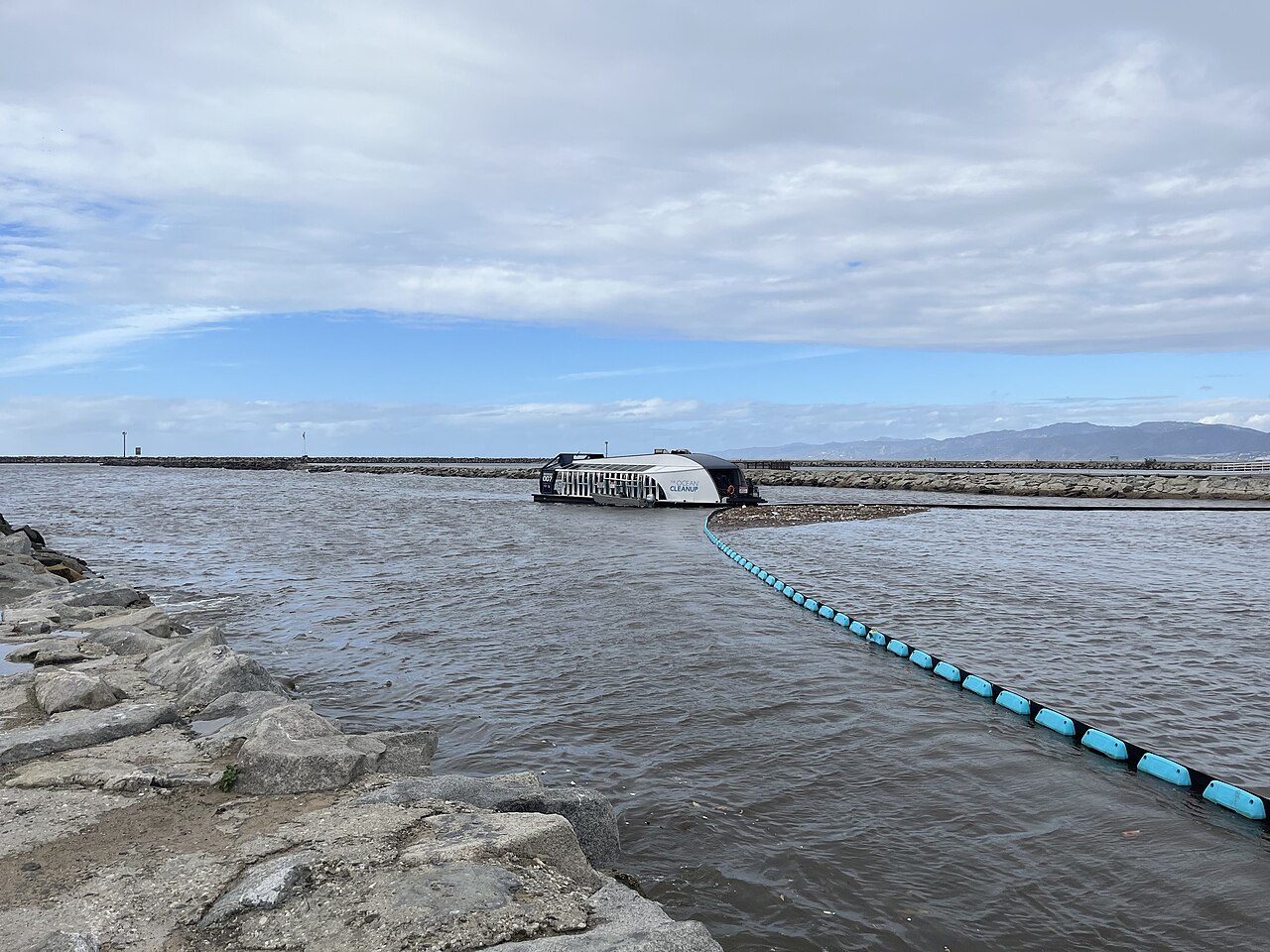 The Ocean Cleanup Interceptor Original in a channel, with a floating boom leading to the catamaran hull