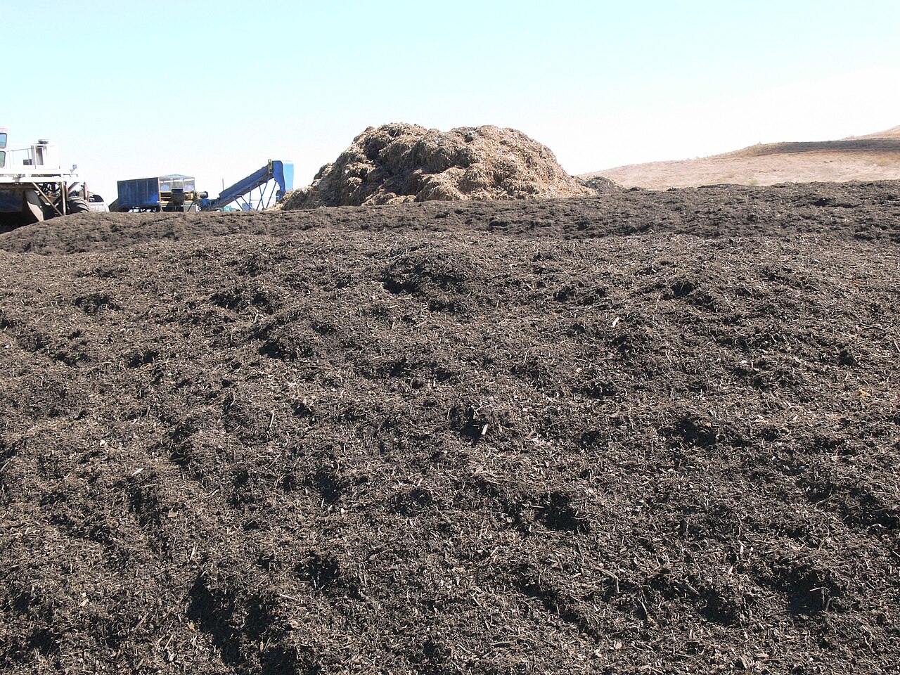 A large pile of finished dark compost at a municipal organics facility, with machinery behind it