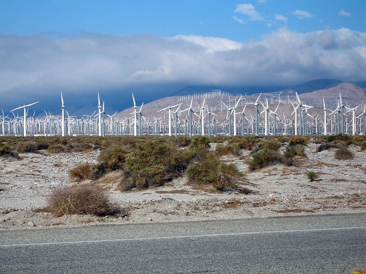 Rows of white onshore wind turbines across a desert plain toward distant mountains