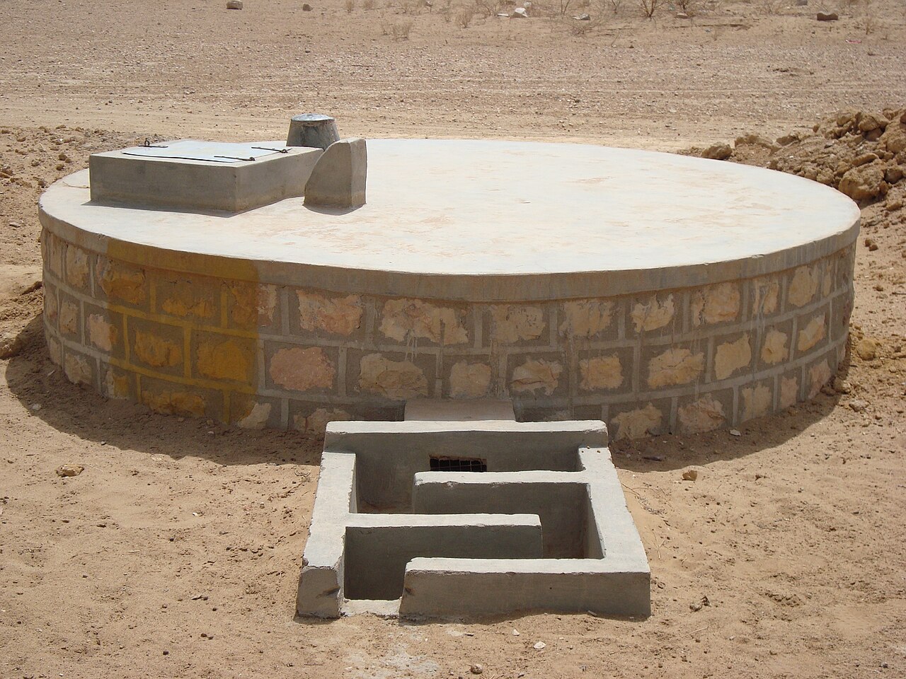A covered masonry rainwater cistern standing in dry ground in India