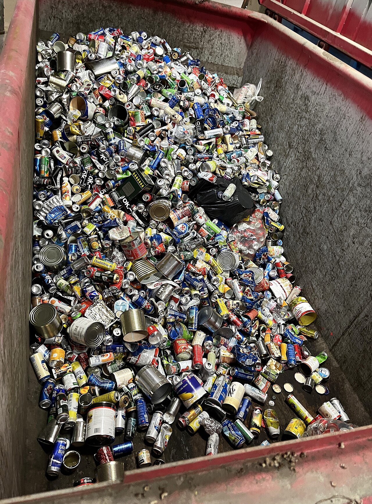 A red collection bin filled with used beverage cans and tins gathered for metal recycling