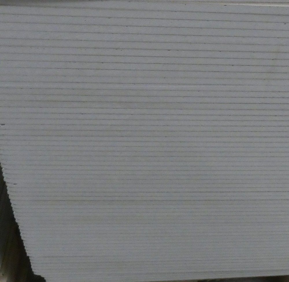 Stack of plasterboard sheets on a wooden pallet in a warehouse.